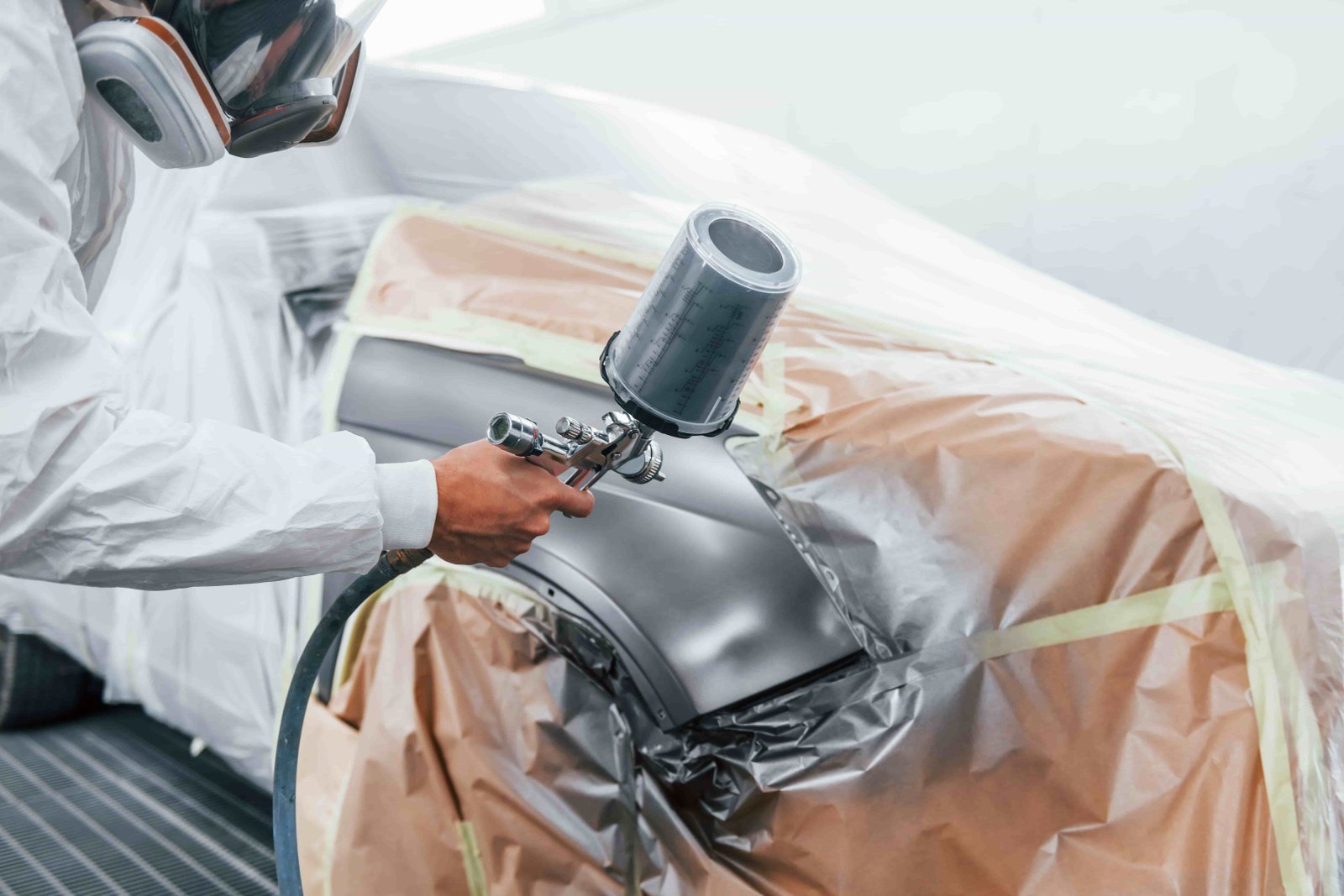 a repairman in uniform paints car in garage