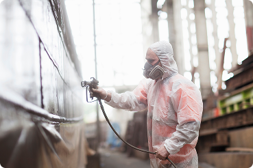 worker spray painting boat in shipyard